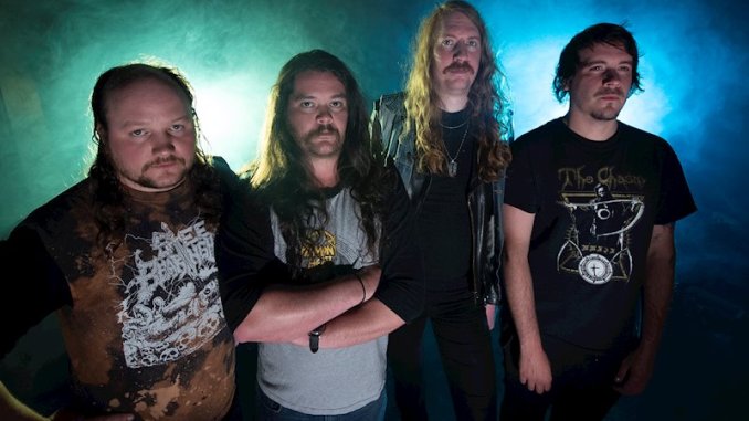 Group photo of Deathblow, a four-member thrash metal band from Utah. The members stand in front of a smoky, blue-lit background, wearing band shirts and long hair. They have serious expressions and a gritty, old-school metal look.