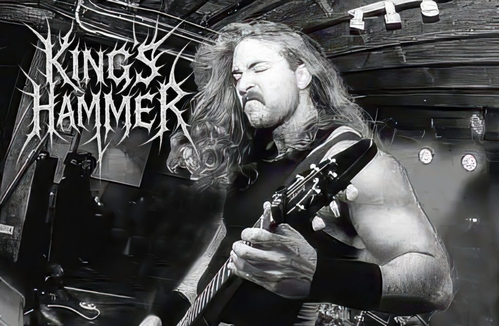 Chuck Weatherman of King’s Hammer playing guitar with intense expression, black tank top, long hair flying mid-performance under dim stage lighting. Band logo appears in jagged white font.