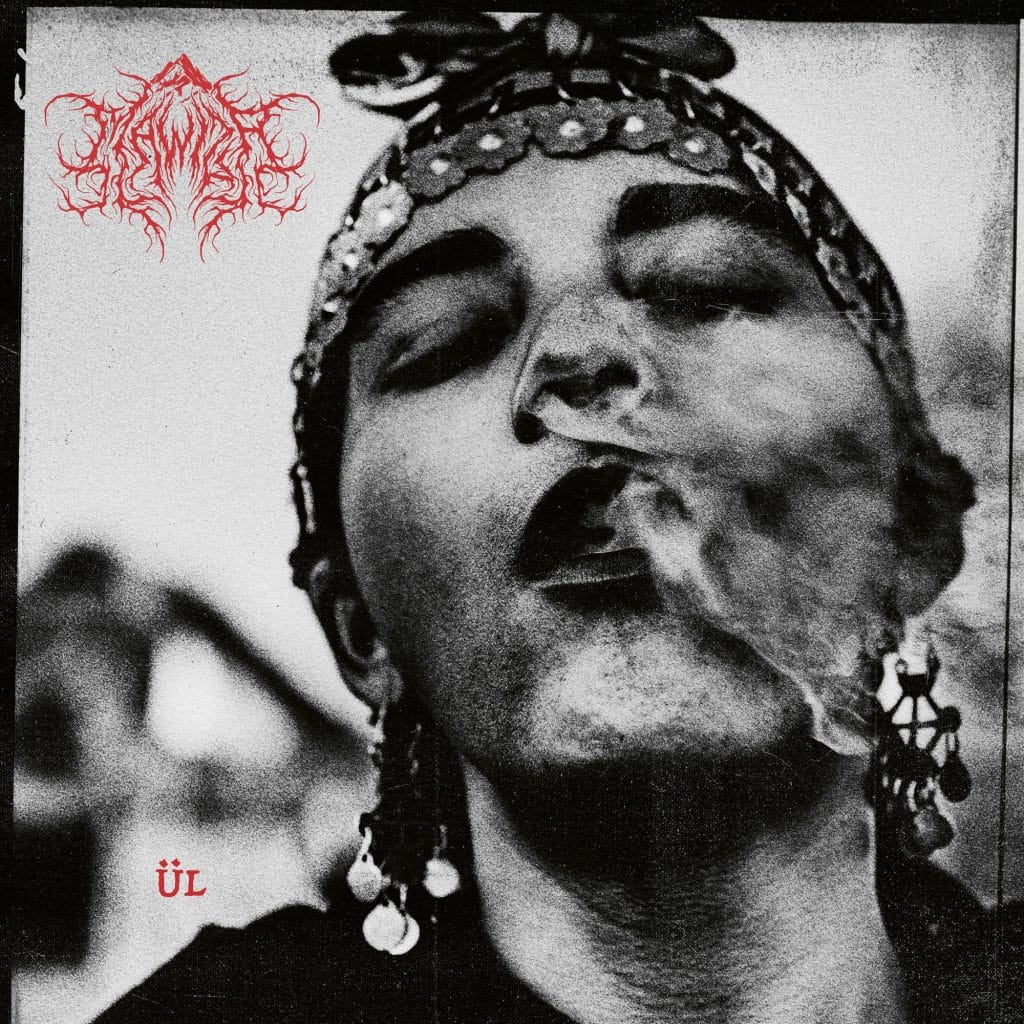 Album cover for ÜL by Mawiza. The black and white image features a grainy, close-up portrait of a person exhaling smoke, their gaze bold and confrontational. They wear a traditional headscarf adorned with coins and jewelry, emphasizing cultural identity and resilience. The band’s raw, red logo appears in the top left corner with jagged, chaotic lettering, while the album title ÜL is printed in simple red font in the bottom left. The overall aesthetic is gritty, rebellious, and steeped in ancestral power.