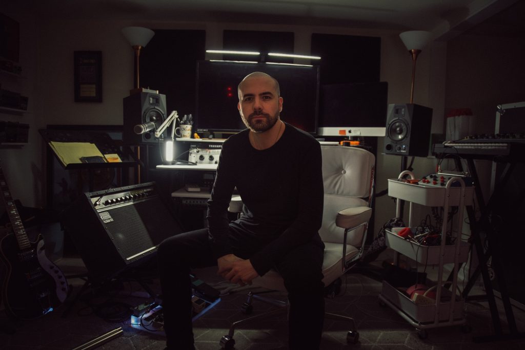 Composer Andrew Gordon Macpherson in studio surrounded by guitars, amps, and gear while scoring Into the Void for Hulu
