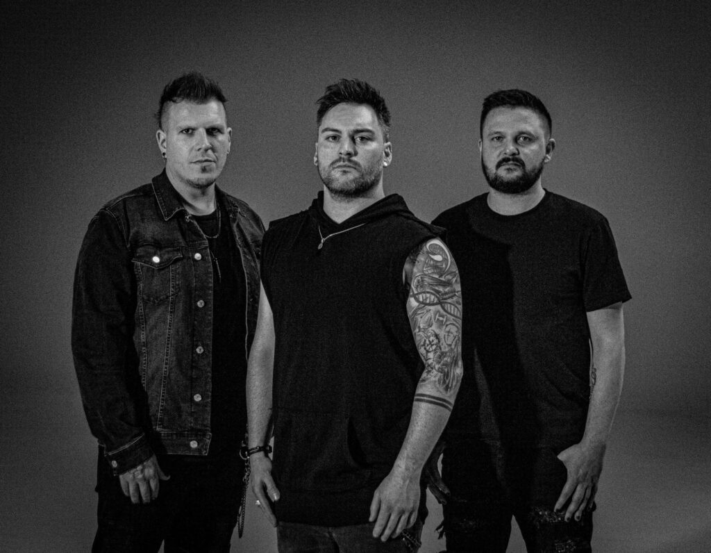 Black and white promo photo of One Last Day featuring vocalist/bassist Huw Roch and guitarists Gareth Stapleton and John Harmsworth standing against a dark backdrop.