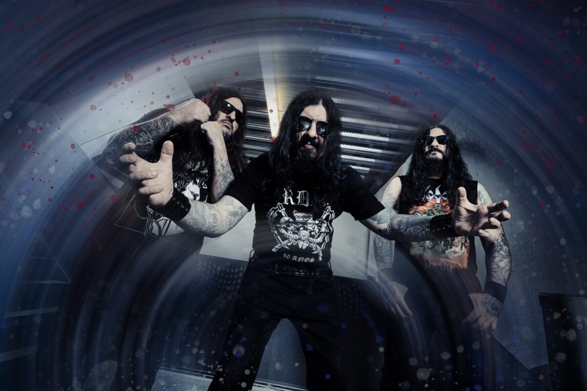 Brazilian death metal band Krisiun standing together in a studio setting, wearing black clothing with serious expressions.