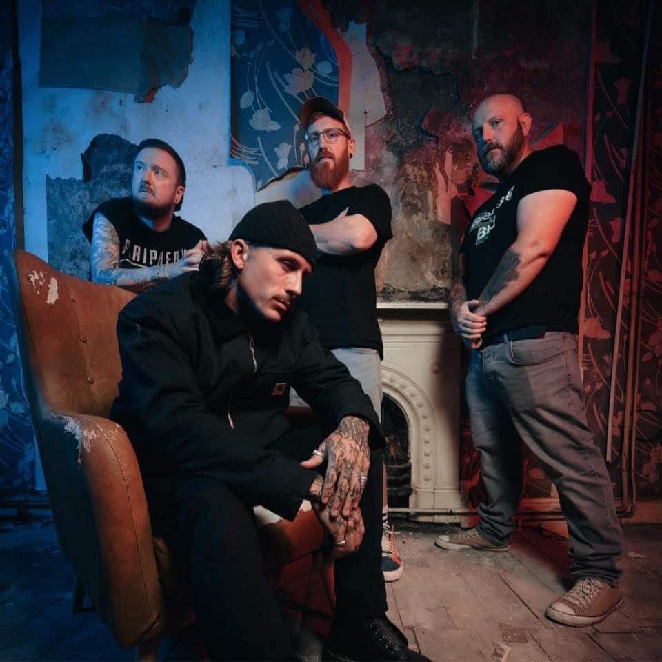 “Edit The Tide band photo with four members in a worn, atmospheric room with blue and red lighting; one seated in a distressed armchair while the others stand behind him.”