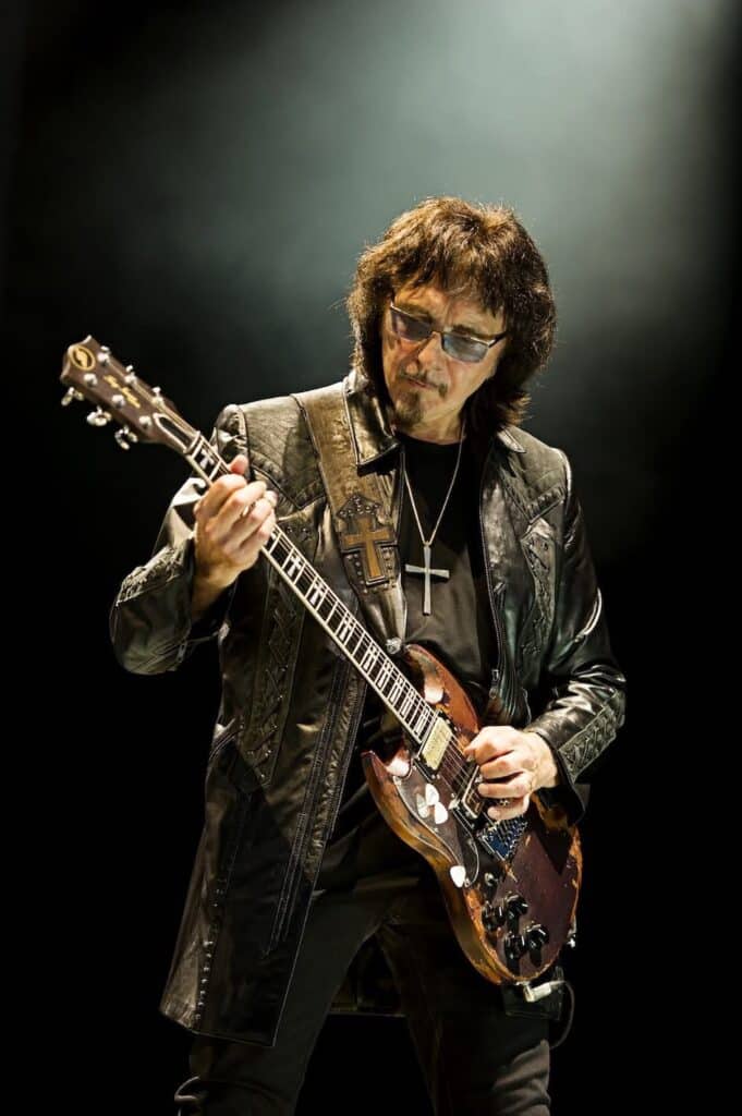 Tony Iommi performing live on stage, playing guitar under dramatic lighting