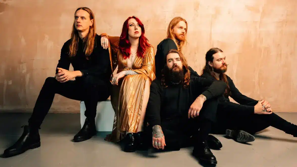 Employed To Serve pose in an orange background with vocalist Justine Jones posing in the center of the UK metalcore band’s lineup.