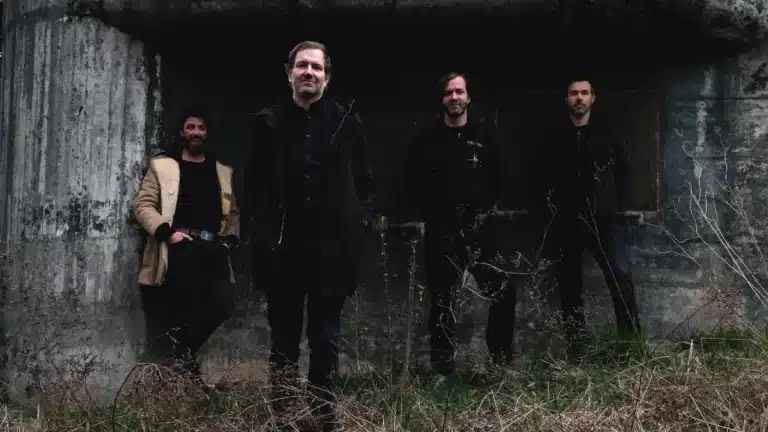 Impure Wilhelmina standing in front of a dark concrete bunker in outdoor promotional photo.