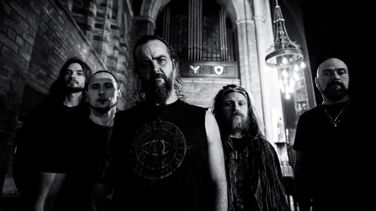 Members of Infected Dead standing inside a gothic church-like hall in black and white promotional photo