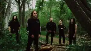 Cattle Decapitation posing in a wooded forest setting during a promotional photo shoot, surrounded by trees and dense greenery.