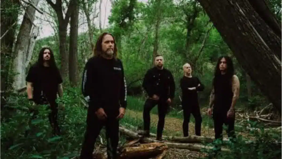 Cattle Decapitation posing in a wooded forest setting during a promotional photo shoot, surrounded by trees and dense greenery.