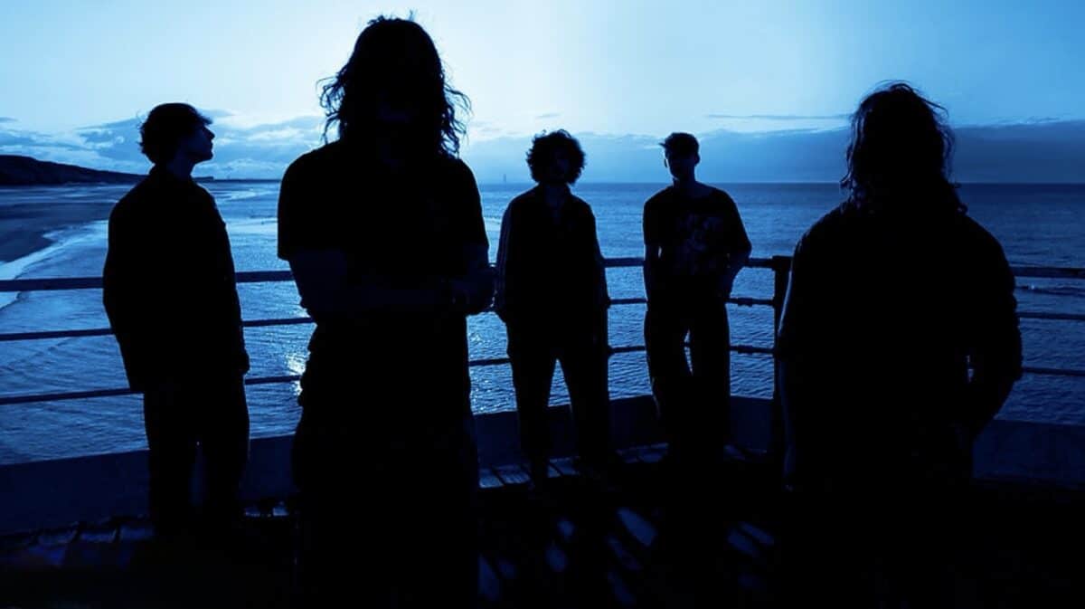 The Larches promotional band photo featuring the five members standing on a seaside pier at dusk.