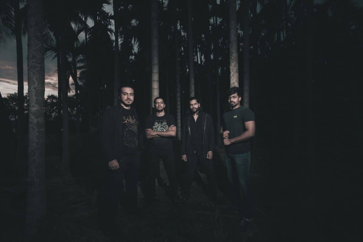 Fallen Letters band members standing among tall palm trees in a dark atmospheric setting