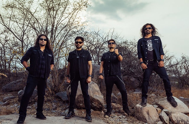 Against Evil band members wearing black and standing on rocks in an outdoor landscape