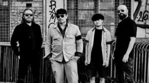 The Konsent interview featured image showing the four members of The Konsent in a black-and-white band portrait outside an industrial graffiti-covered building.