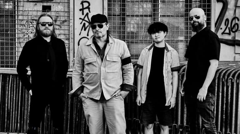 The Konsent interview featured image showing the four members of The Konsent in a black-and-white band portrait outside an industrial graffiti-covered building.