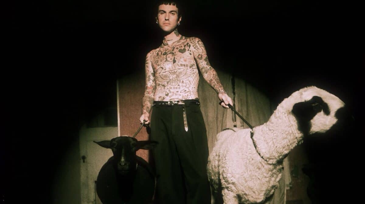 Jutes Love Psychosis promotional image showing tattooed alternative rock musician Jordan Lutes standing shirtless between a black sheep and a white sheep against a dark background.