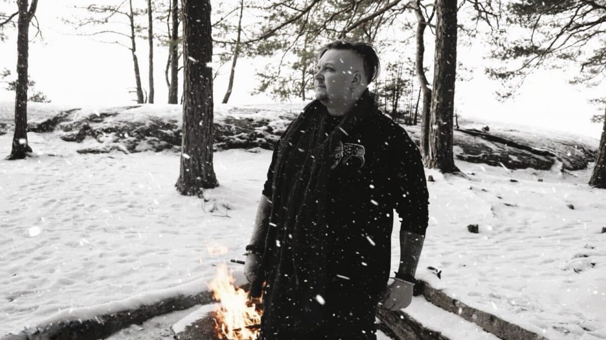 ISVIDD Interview featuring Björn standing in a snow-covered Swedish forest beside a small fire.