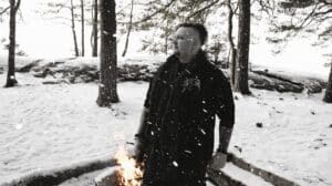 ISVIDD Interview featuring Björn standing in a snow-covered Swedish forest beside a small fire.