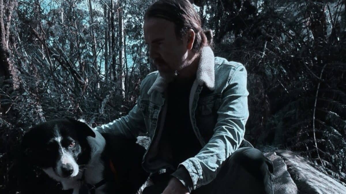 Craig Bannerman Interview featured photograph of the Australian extreme metal musician crouching beside his black-and-white dog in a wooded landscape.