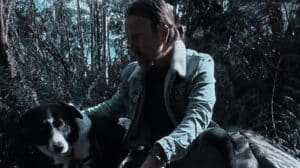 Craig Bannerman Interview featured photograph of the Australian extreme metal musician crouching beside his black-and-white dog in a wooded landscape.
