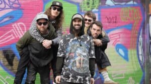 Look What Happened Weak Minds for the Weekend review – Brighton pop-punk band posing together in front of a colorful graffiti wall.